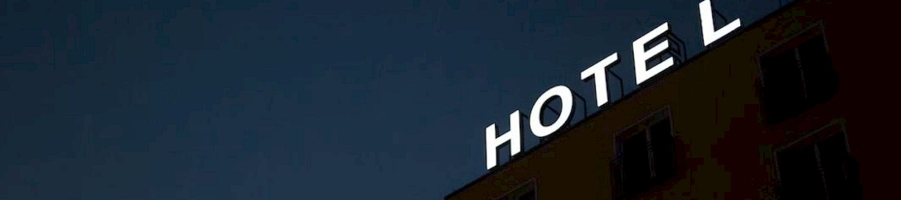 The image shows the top corner of a building at night with an illuminated "HOTEL" sign, where the letter "L" appears to be slightly tilted.