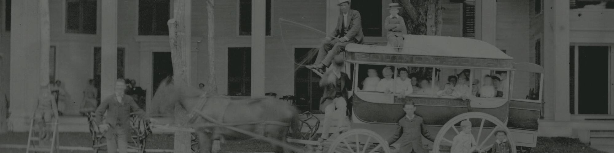 A vintage photo depicts a horse-drawn carriage with passengers and a driver, in front of a large building, possibly a hotel or residence, ending the sentence.