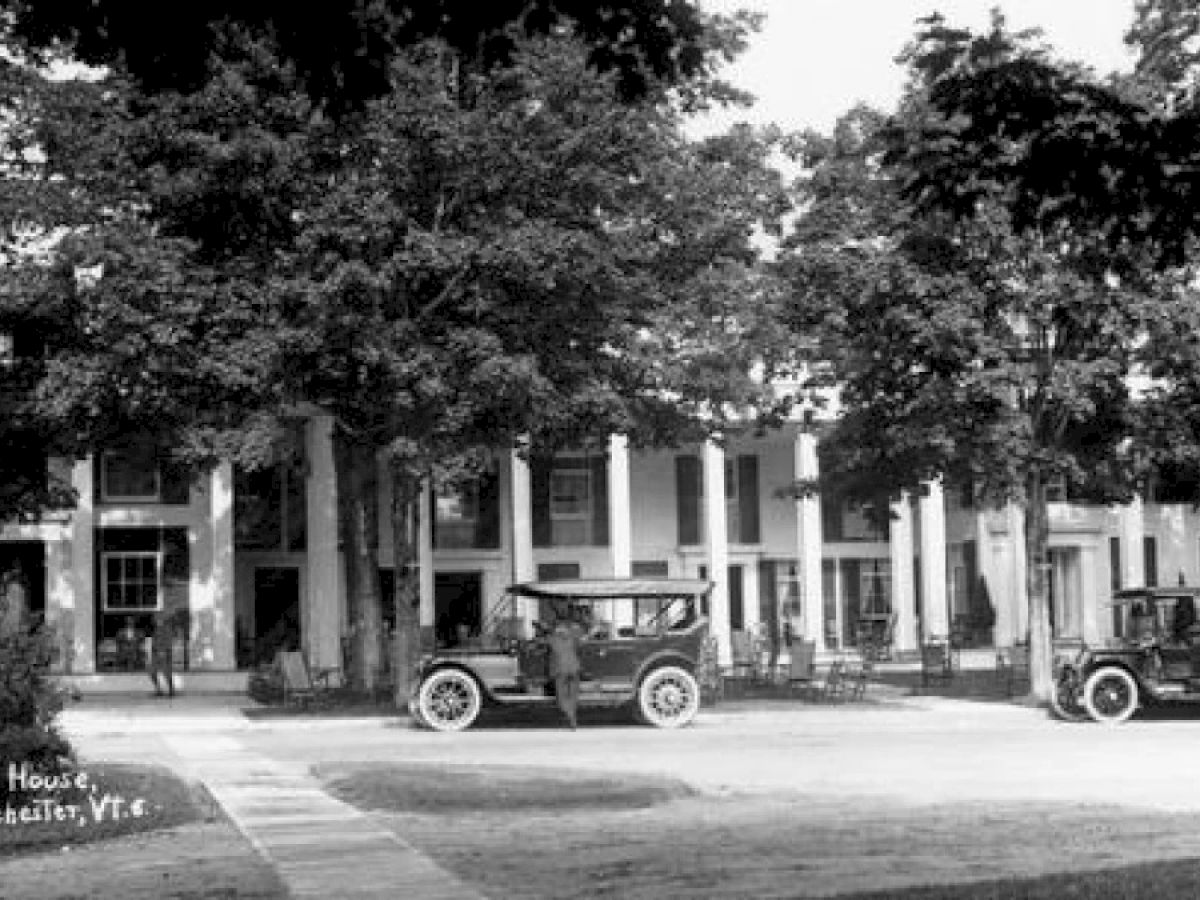 A vintage scene of a columned building surrounded by trees with two early 20th-century cars parked in front, labeled "Equinox House, Manchester, VT."