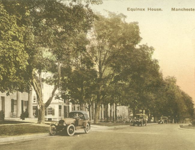 A vintage postcard shows a street with classic cars, trees, and the Equinox House in Manchester, Vermont.