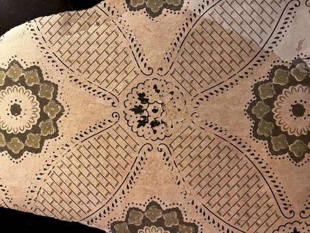 A patterned beige fabric with a retro floral and lattice design, featuring symmetric flowers in green and cream hues across a quilted backdrop.