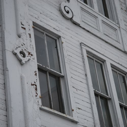 Worn white building facade with peeling paint, barred windows, and decorative address numbers &ldquo;6&rdquo; and &ldquo;9&rdquo;.